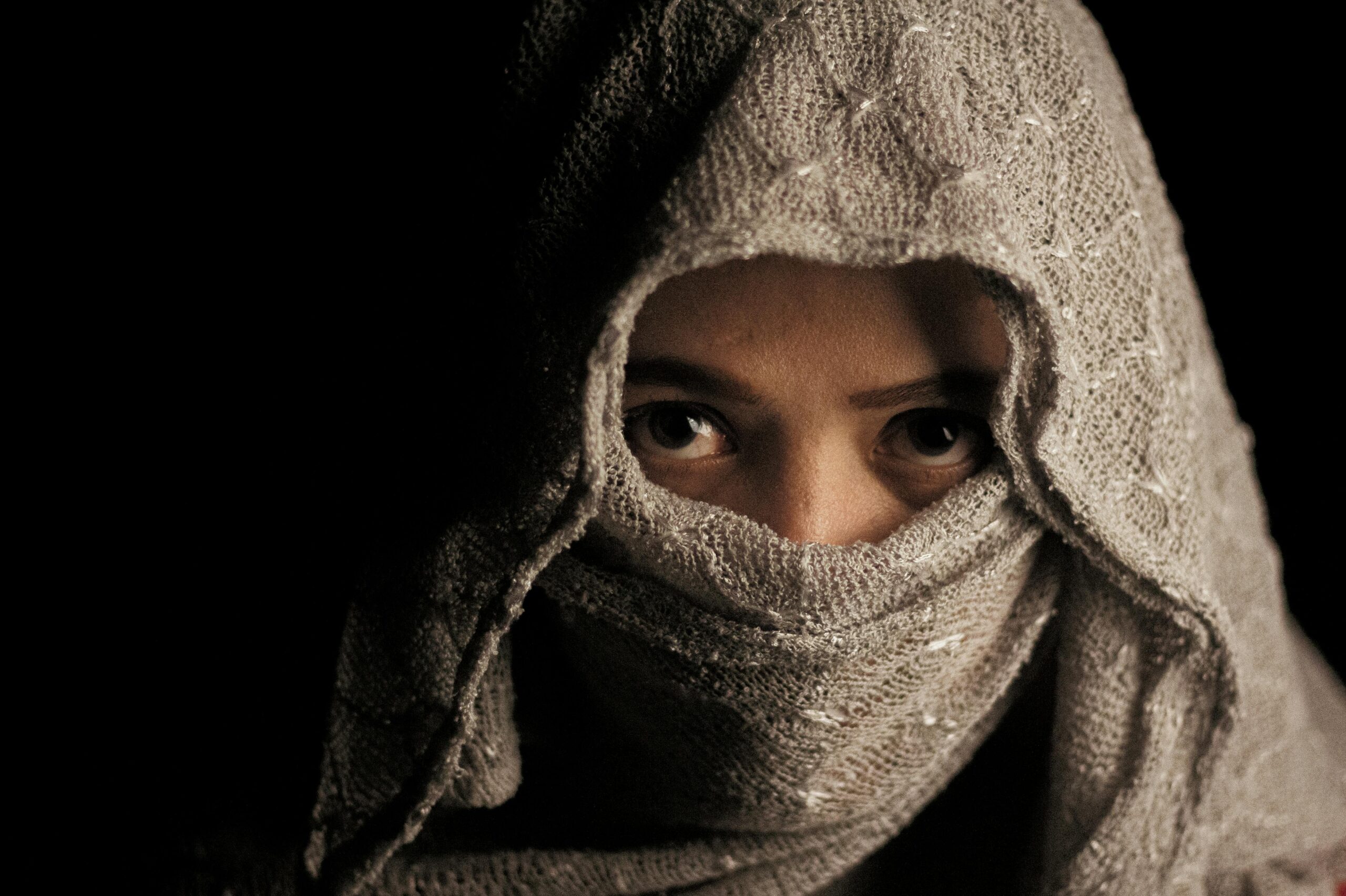 Close-up portrait of a woman with wool fabric covering her face, only eyes visible.